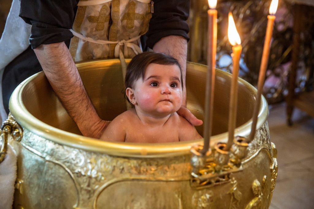 A baby being bathed at a Greek christening photographer, twelve apostles church, brookmans Park, Hertfordshire