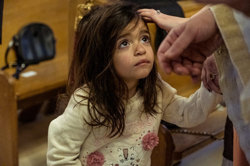 little girl looks up at priest at greek christening