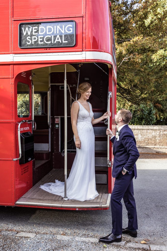 Bride and groom pose on red bus outside hertfordshire pub wedding