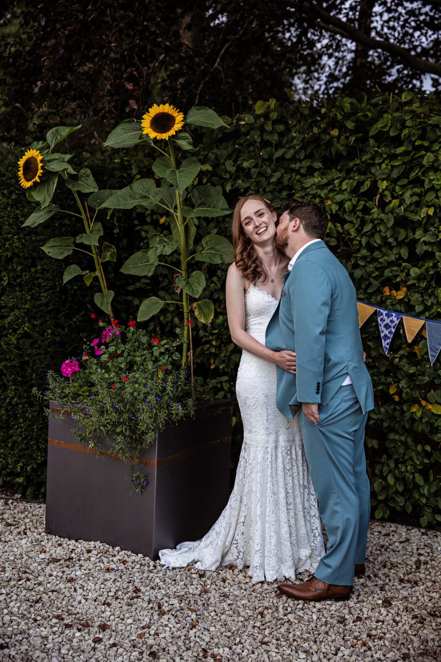 the bride and groom pose for picture in their garden with flowers in foreground