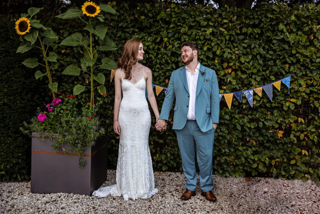 Hertfordshire wedding photography, Bride and groom hold hands in a floral garden with colourful bunting 