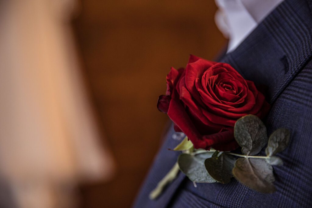 a details picture of a red rose button hole at a hertfordshire wedding