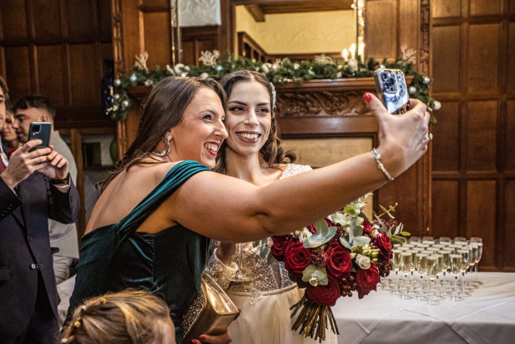 a bride poses with her guest as she takes a phone selfie at Fanhams Hall