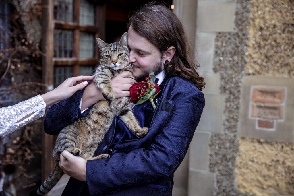 A groom cuddles a cat at Fanhams Hall at his wedding in December