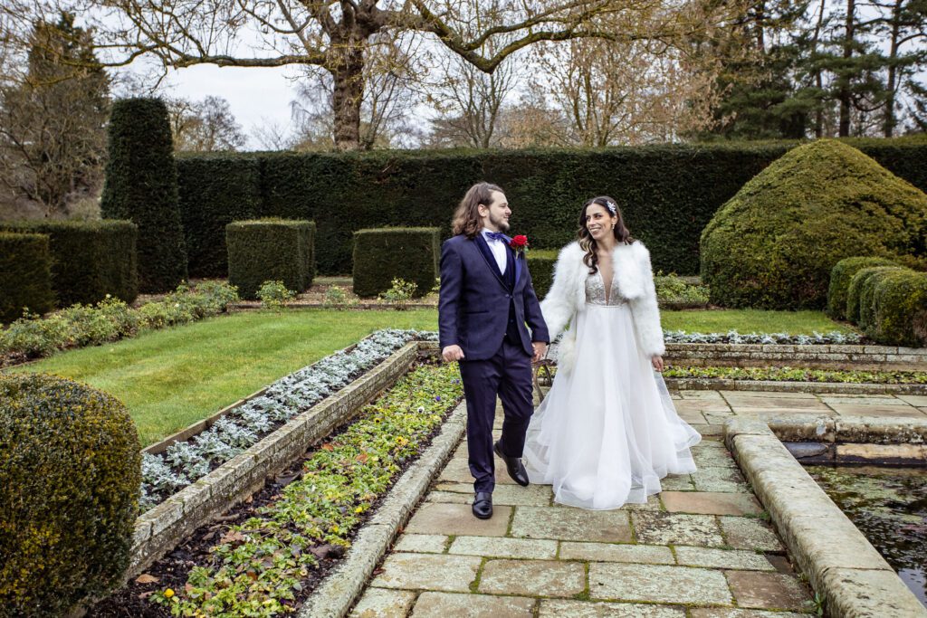 A bride and groom walk in the gardens of Fanhams Hall hand in hand