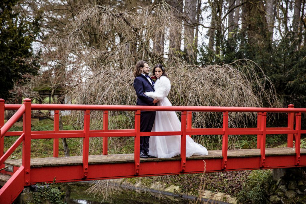 bride and groom pose on red bridge at fanhams Hall Hertfordshire wedding. Photography by Natalie Martinez