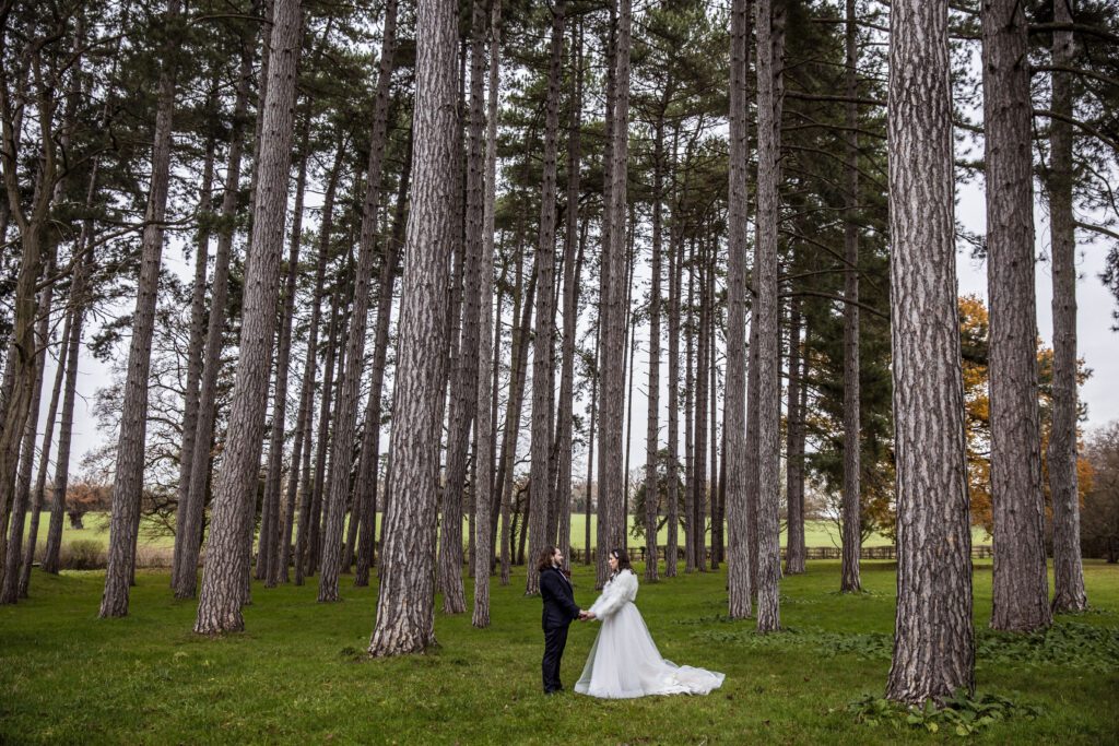 A bride and groom hold hands as they pose in the forest at Fanhams Hall in Hertfordshire