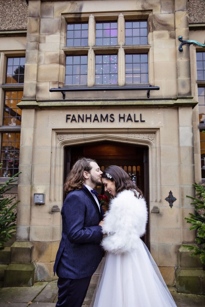 A bride and groom kiss in the doorway of Fanhams Hall at their wedding in December