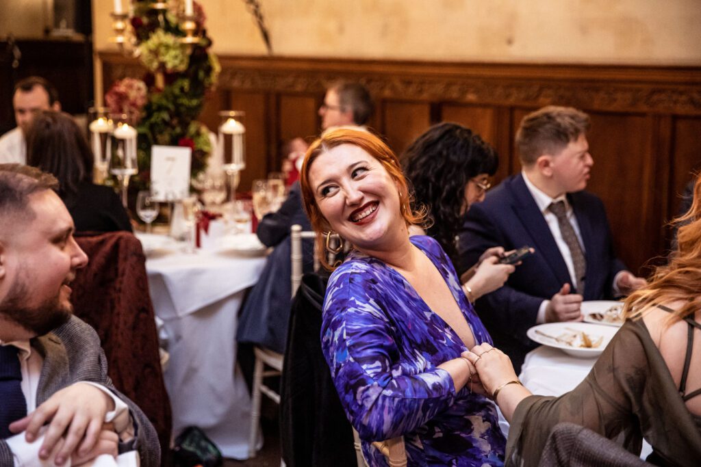 A red haired guest talks to another guest while seated at a table at a wedding at Fanhams Hall in Hertfordshire