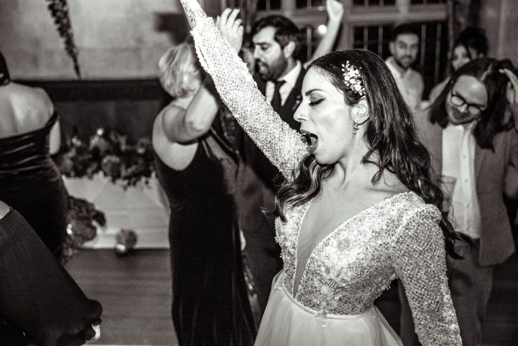 A bride sings loudly on the dance floor, her hand is in the air. Photography by Natalie Martinez
