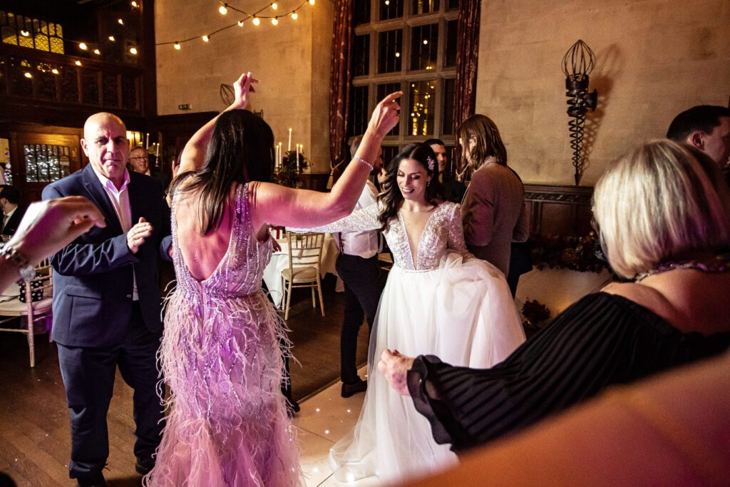 Guests dance a greek dance with hands in the air at a wedding at Fanhams Hall
